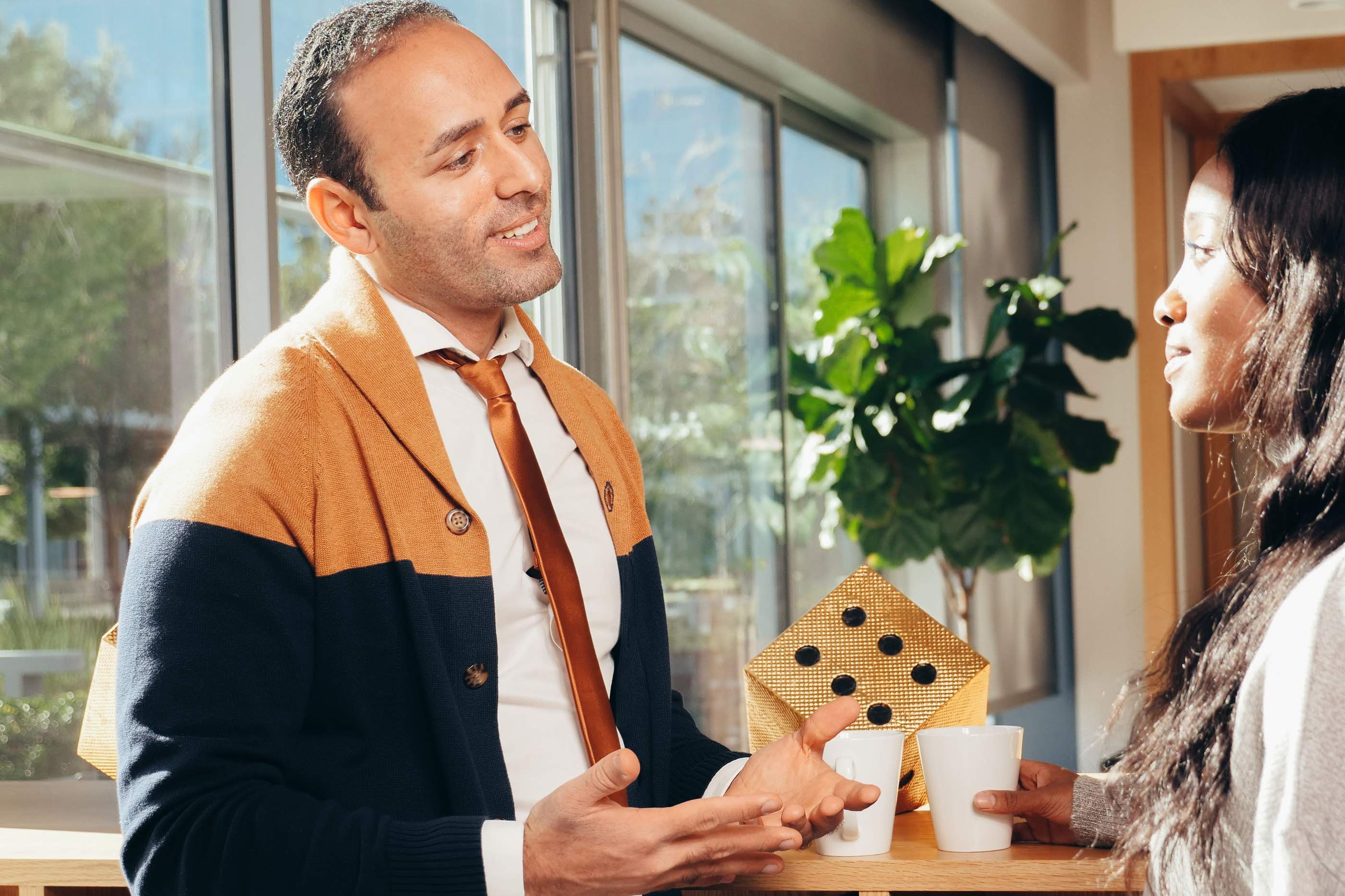 Two colleagues in conversation over coffee beside an office window